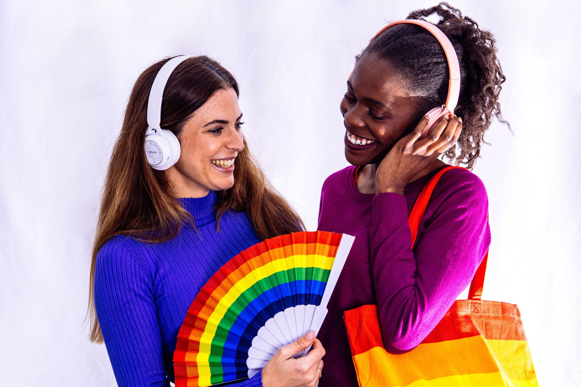 Two smiling young women listening music with headphones and rainbow fan